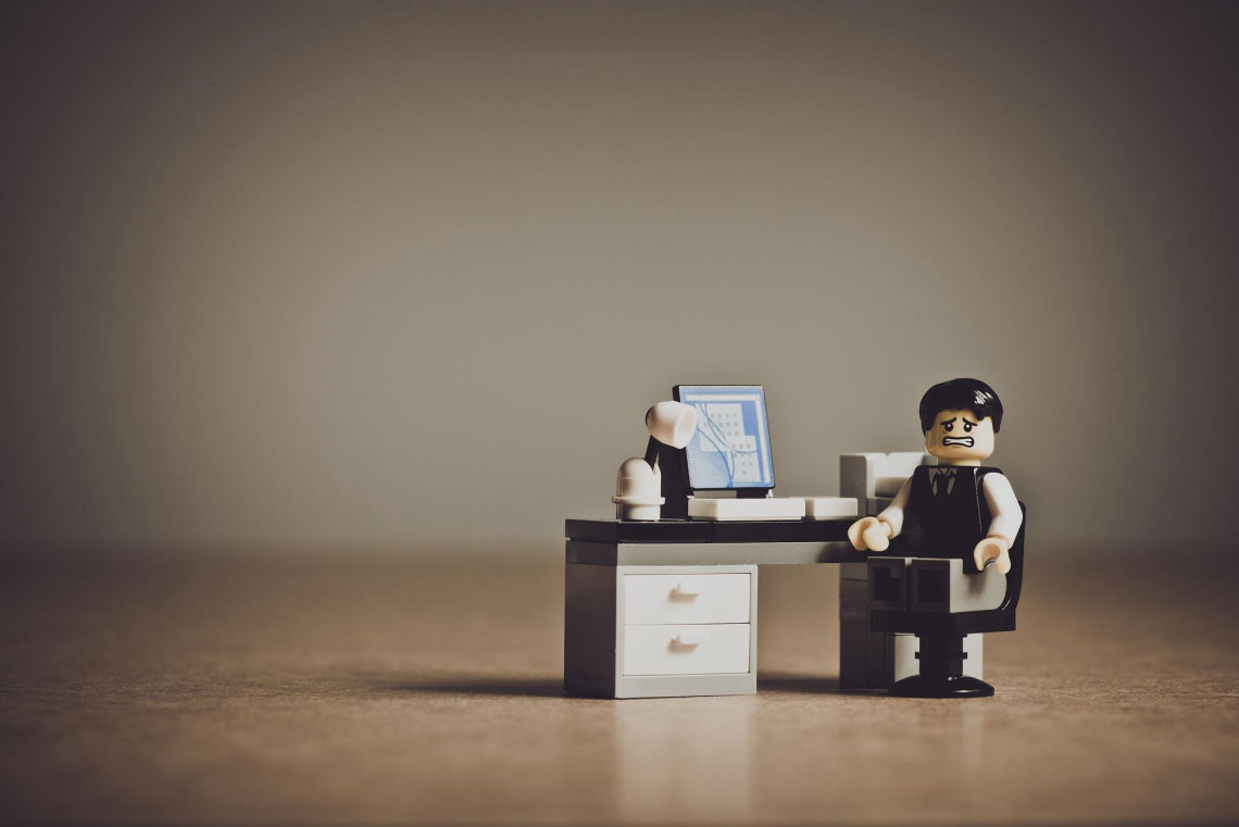 A Lego figure character sits in an office with a face of despair