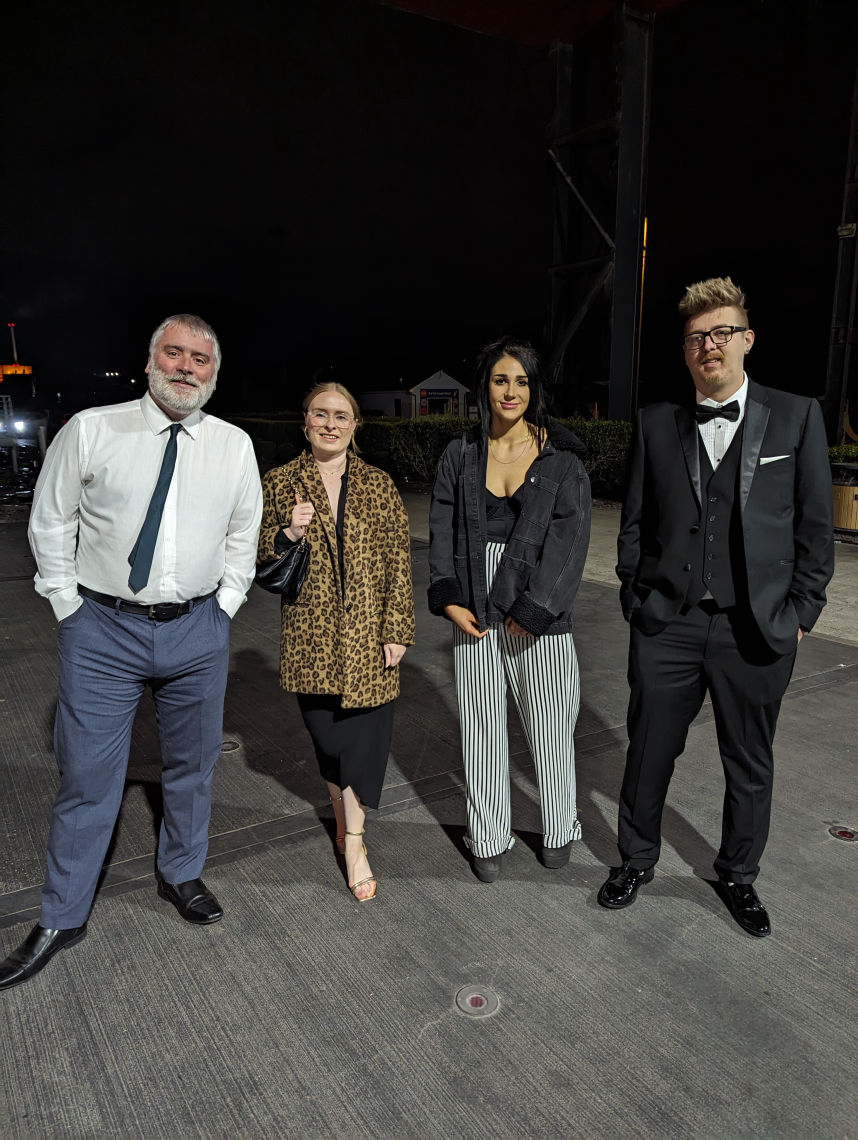 Four people (two men and two women) dressed smartly pose outside an awards venue